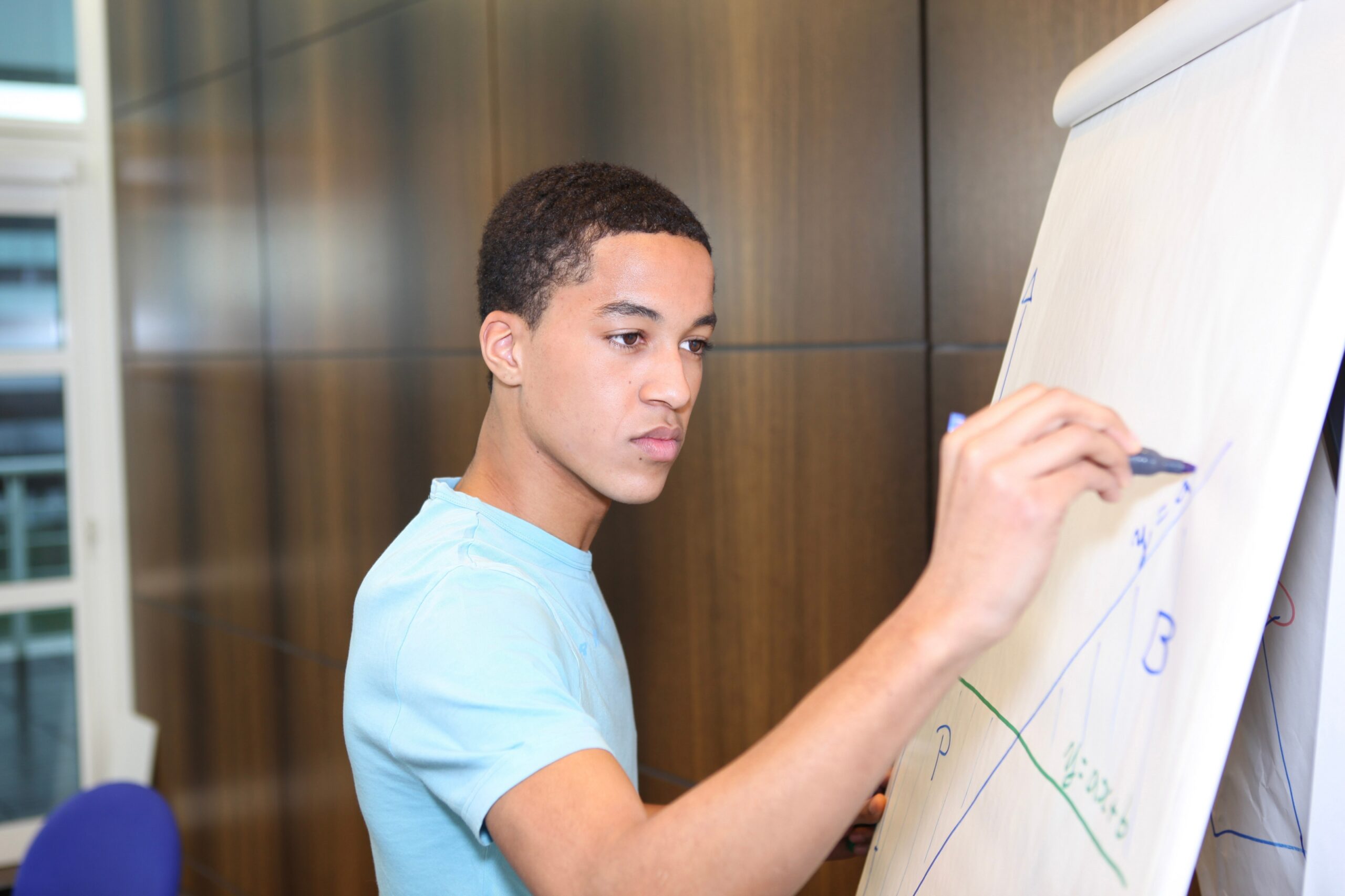 A young man is actively writing on a whiteboard, demonstrating engagement in a learning or brainstorming session.
