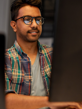 A man in glasses and a plaid shirt is focused on his work at a computer, showcasing a professional environment.