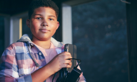 A young boy is holding a cell phone, looking intently at the screen with a focused expression on his face.