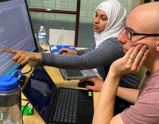 Two individuals collaborating on a computer, focused on the monitor in front of them, engaged in productive work.