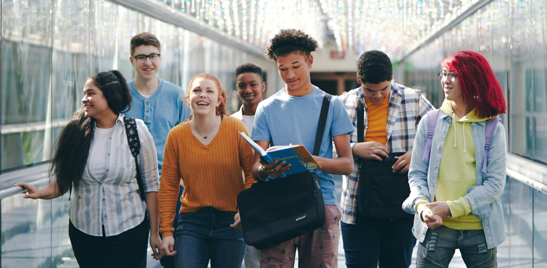 A diverse group of young individuals walking together down a brightly lit hallway, engaged in conversation and laughter.
