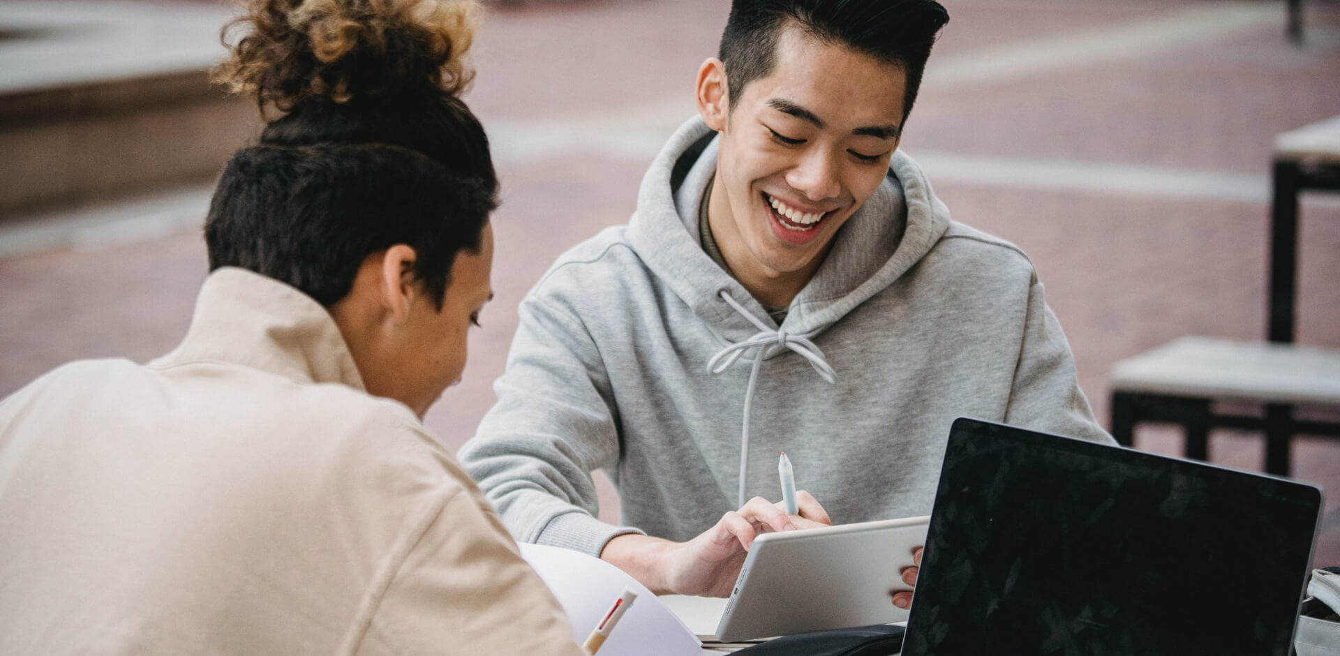 Two students collaborate at a table, focused on a laptop, engaged in their studies.