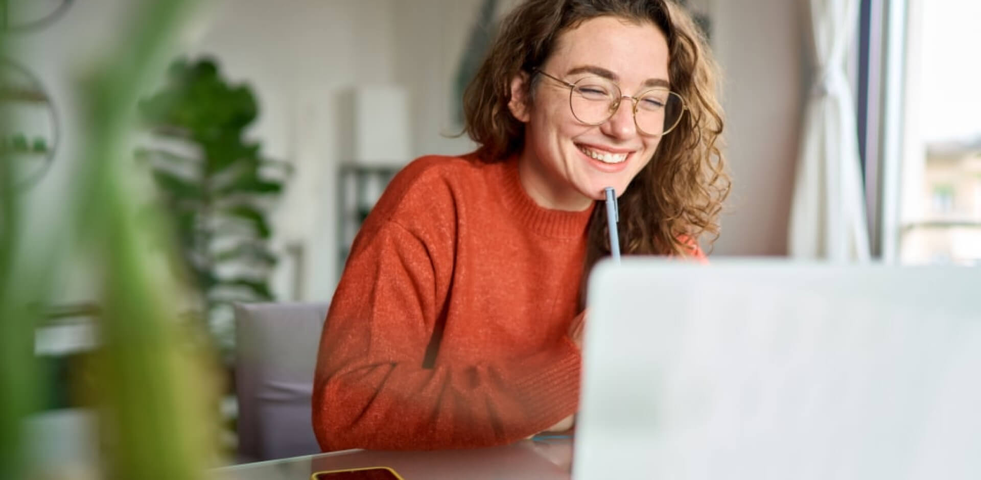 A smiling woman wearing glasses is engaged with her laptop, showcasing a moment of productivity and joy.