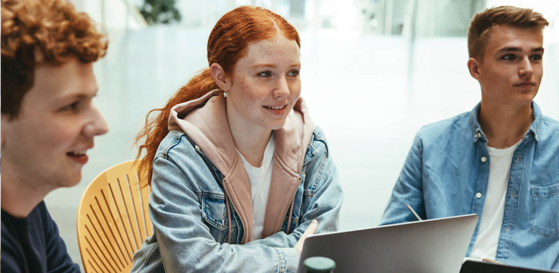 Three young individuals engaged in work at a table, each using their laptops for collaborative tasks.