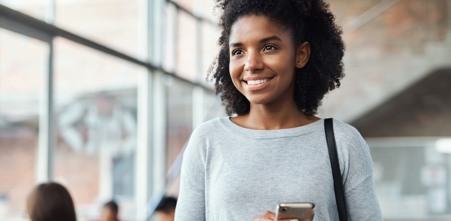 A woman with curly hair is holding a cell phone, looking engaged and focused on her device.