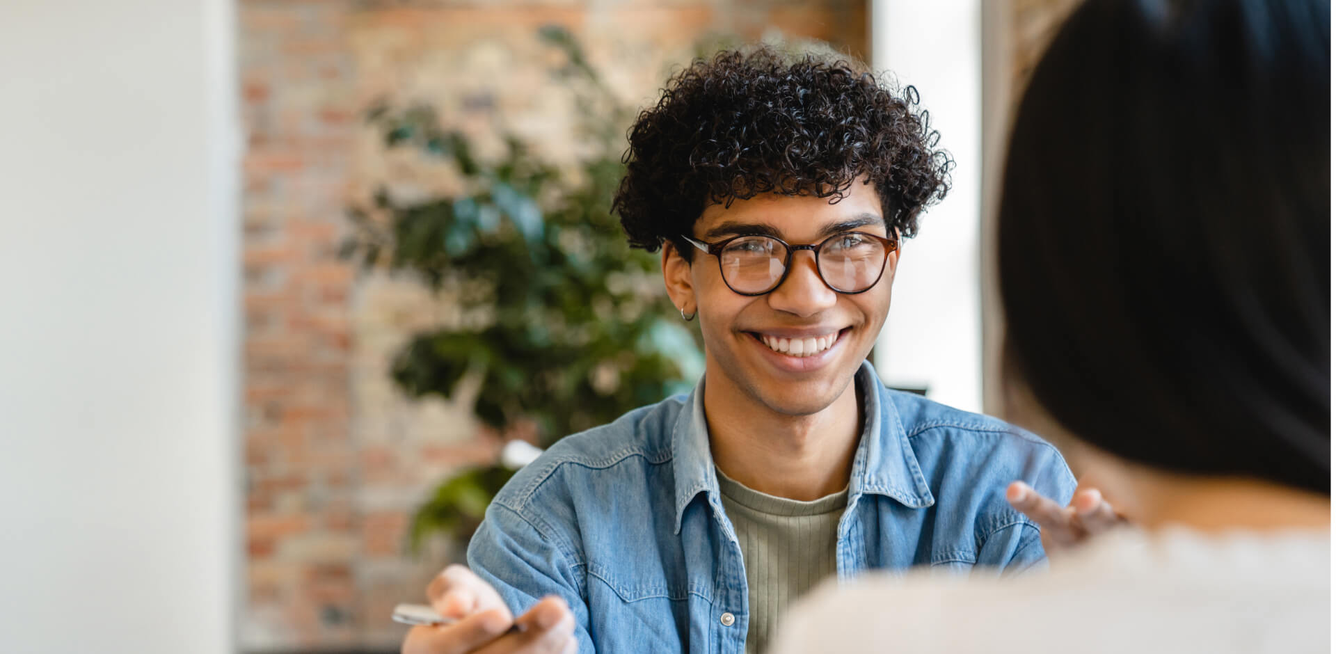 A man wearing glasses engages in conversation with a woman, both appearing attentive and engaged in dialogue.
