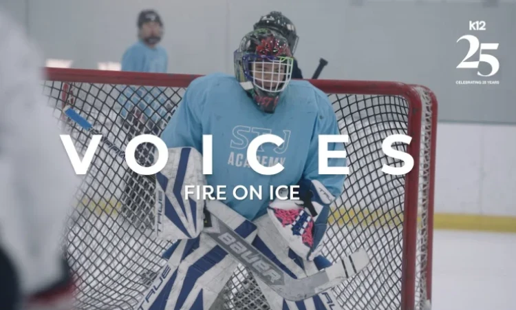 A hockey goalie in a blue jersey and colorful helmet stands guard by a net on the ice rink. Text reads “Voices: Fire on Ice.” Atmosphere is focused and energetic.
